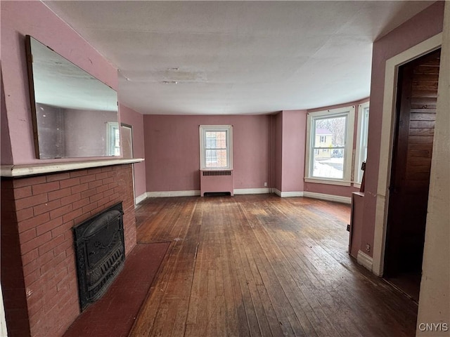 unfurnished living room featuring radiator, hardwood / wood-style floors, and a brick fireplace