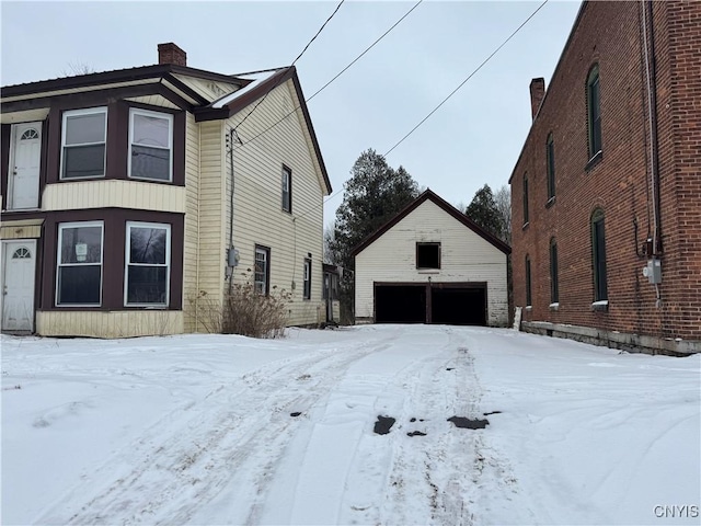 view of snow covered exterior featuring a garage and an outbuilding