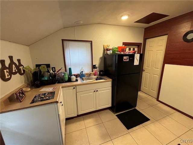 kitchen featuring sink, light tile patterned floors, black fridge, lofted ceiling, and white cabinets