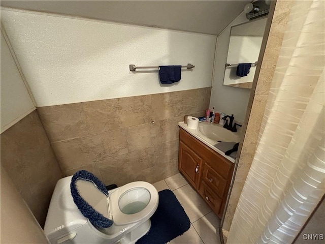 bathroom with vanity, lofted ceiling, tile patterned flooring, toilet, and tile walls