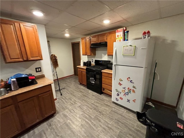 kitchen with black gas range, a drop ceiling, and white fridge