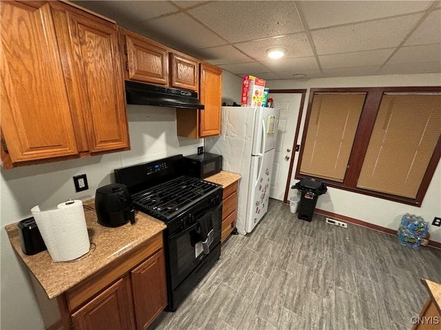 kitchen featuring light wood-type flooring, black gas range, a paneled ceiling, and white fridge