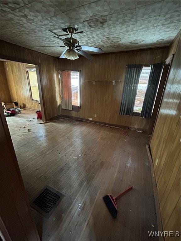 unfurnished room featuring hardwood / wood-style flooring, ceiling fan, and wooden walls