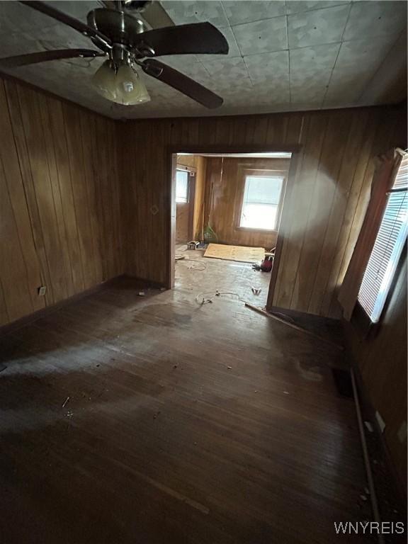 empty room with ceiling fan, dark hardwood / wood-style flooring, and wooden walls