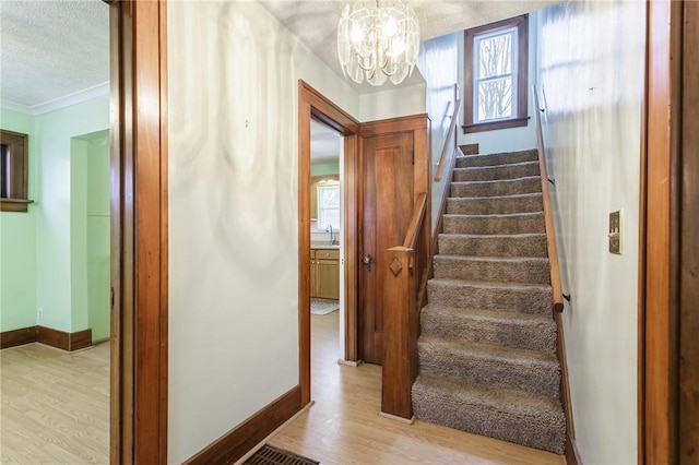 staircase featuring ornamental molding, a chandelier, a textured ceiling, and wood-type flooring