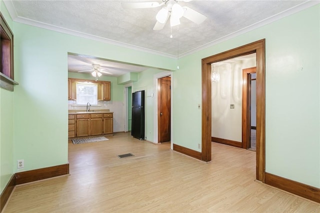 interior space with sink, black fridge, light hardwood / wood-style flooring, crown molding, and a textured ceiling