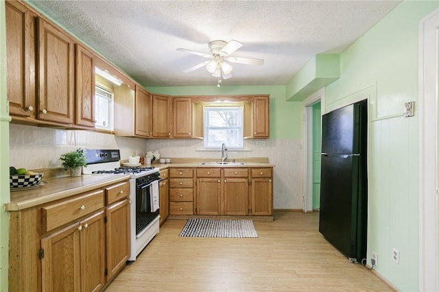 kitchen with ceiling fan, sink, light hardwood / wood-style flooring, white range with gas cooktop, and black refrigerator