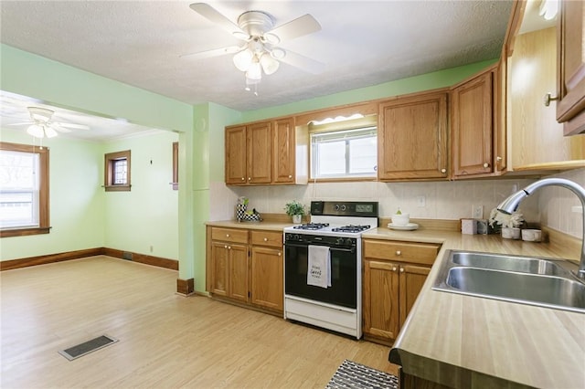 kitchen with white stove, light hardwood / wood-style floors, a healthy amount of sunlight, and sink