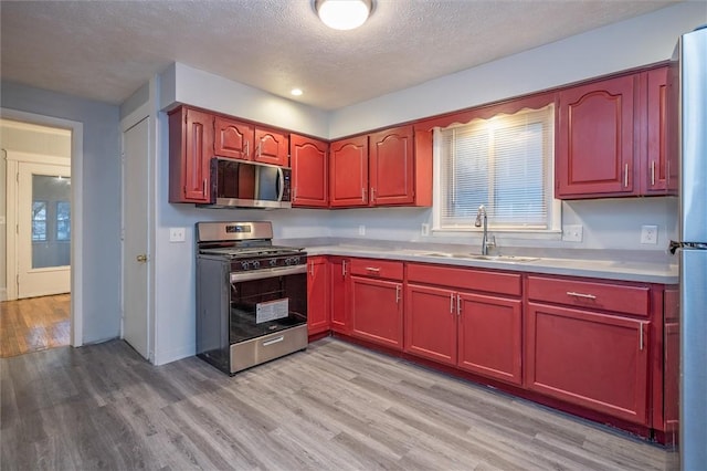 kitchen featuring a textured ceiling, stainless steel appliances, light hardwood / wood-style floors, and sink