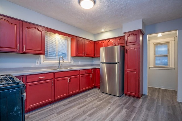 kitchen with stainless steel fridge, black stove, a textured ceiling, sink, and light hardwood / wood-style flooring