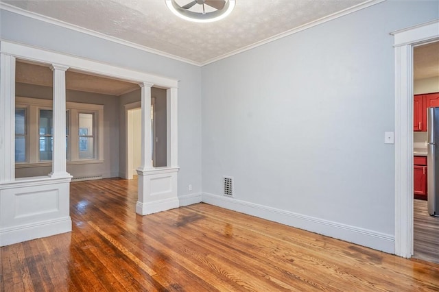 spare room featuring a textured ceiling, hardwood / wood-style flooring, decorative columns, and ornamental molding