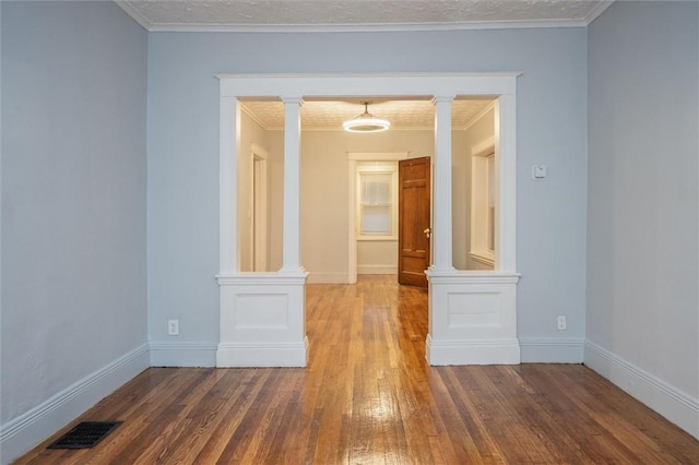 unfurnished room featuring wood-type flooring, ornamental molding, and decorative columns