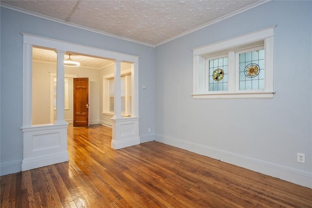 spare room with dark hardwood / wood-style floors, ornamental molding, a textured ceiling, and ornate columns