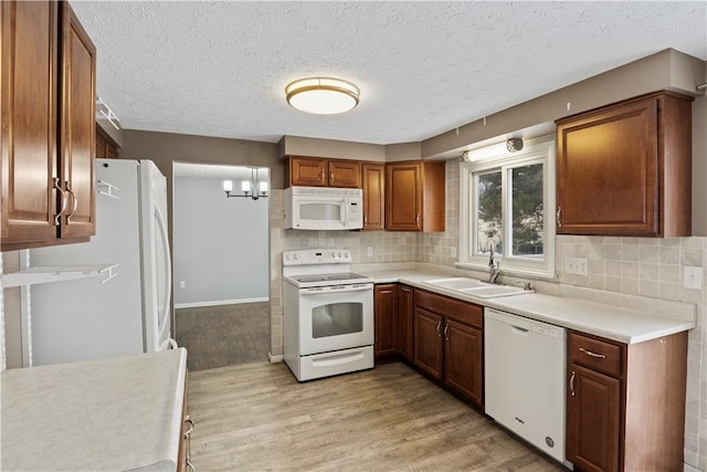 kitchen featuring backsplash, white appliances, sink, an inviting chandelier, and light hardwood / wood-style floors