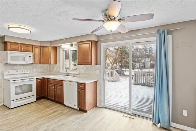 kitchen featuring sink, tasteful backsplash, light hardwood / wood-style floors, a textured ceiling, and white appliances