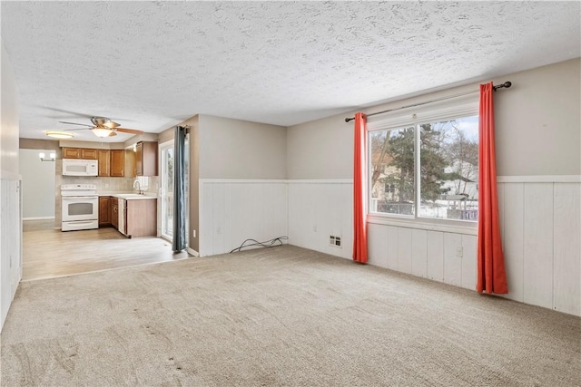 unfurnished living room with a textured ceiling, ceiling fan, light colored carpet, and sink