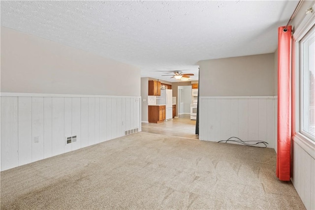 empty room with ceiling fan, a textured ceiling, and light carpet