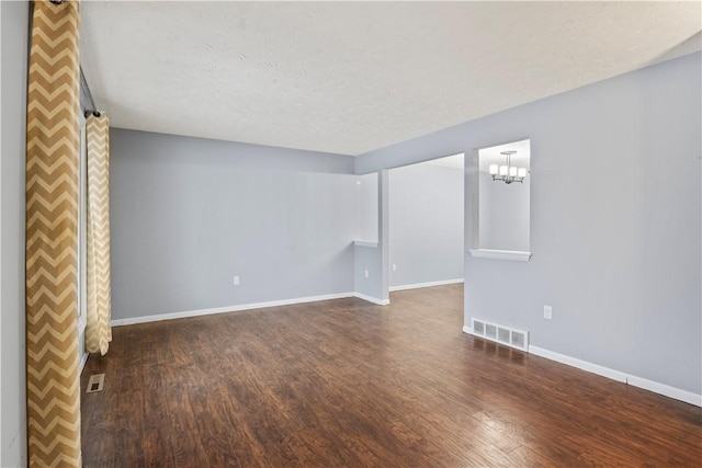 empty room with a textured ceiling, dark hardwood / wood-style floors, and a notable chandelier