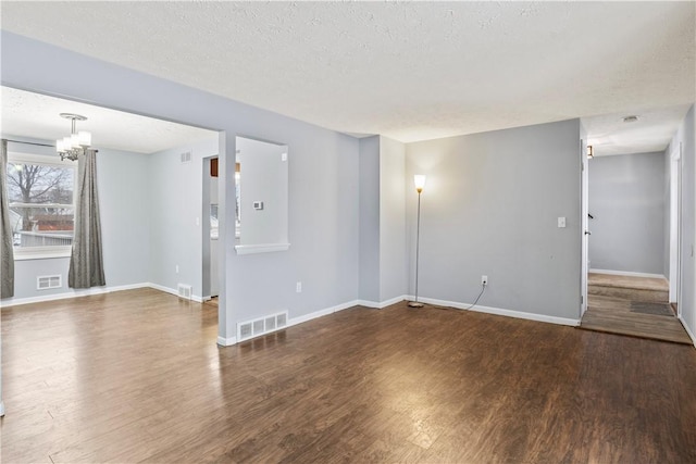 empty room with dark hardwood / wood-style flooring, a textured ceiling, and an inviting chandelier