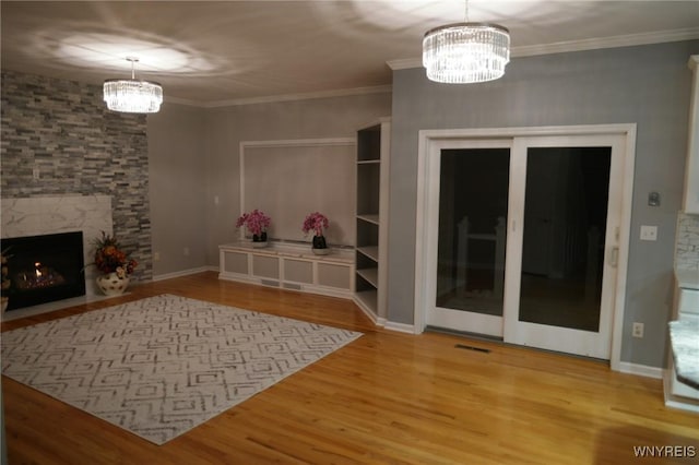 unfurnished living room with a notable chandelier, wood-type flooring, a premium fireplace, and crown molding