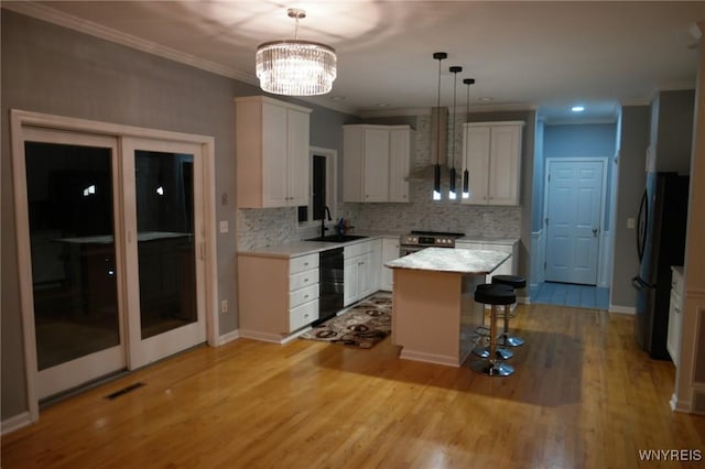 kitchen featuring wall chimney range hood, a kitchen island, pendant lighting, white cabinets, and black appliances