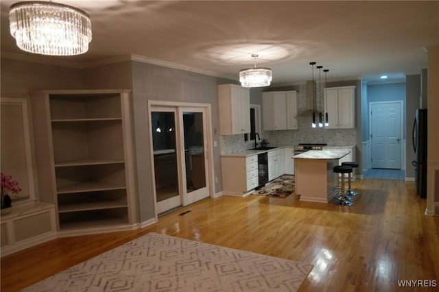 kitchen with a breakfast bar, wall chimney range hood, sink, white cabinets, and a center island