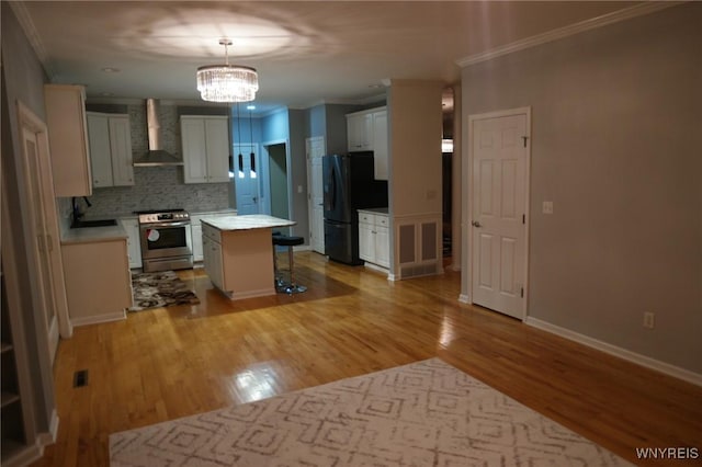 kitchen with black fridge, stainless steel range, wall chimney range hood, a kitchen island, and hanging light fixtures