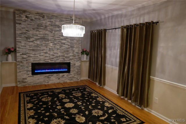 interior space featuring a stone fireplace, hardwood / wood-style floors, ornamental molding, and an inviting chandelier