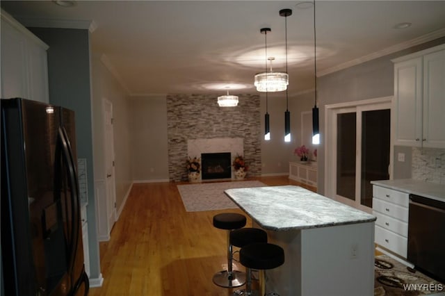 kitchen featuring pendant lighting, a center island, black appliances, white cabinets, and a kitchen bar