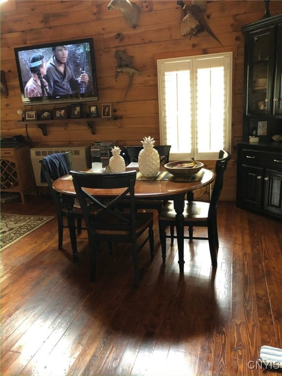 dining space with dark hardwood / wood-style flooring and wooden walls