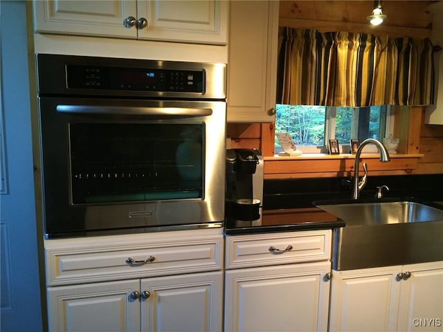 kitchen with sink, tasteful backsplash, white cabinetry, and stainless steel oven