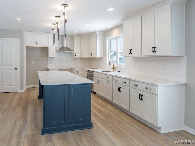 kitchen featuring a center island, decorative light fixtures, wall chimney range hood, white cabinets, and sink