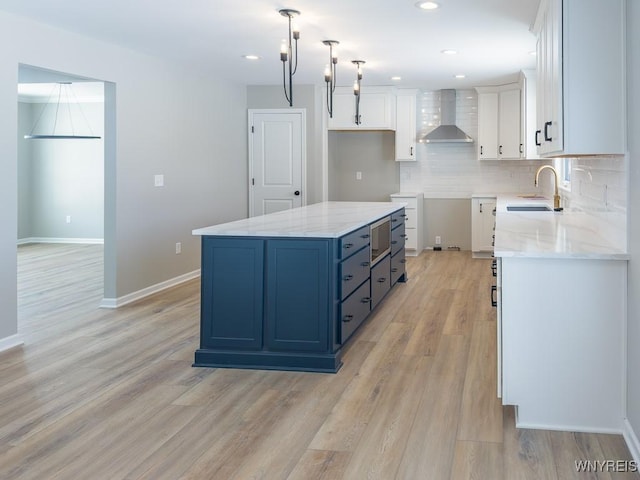 kitchen featuring wall chimney range hood, pendant lighting, a center island, sink, and white cabinetry