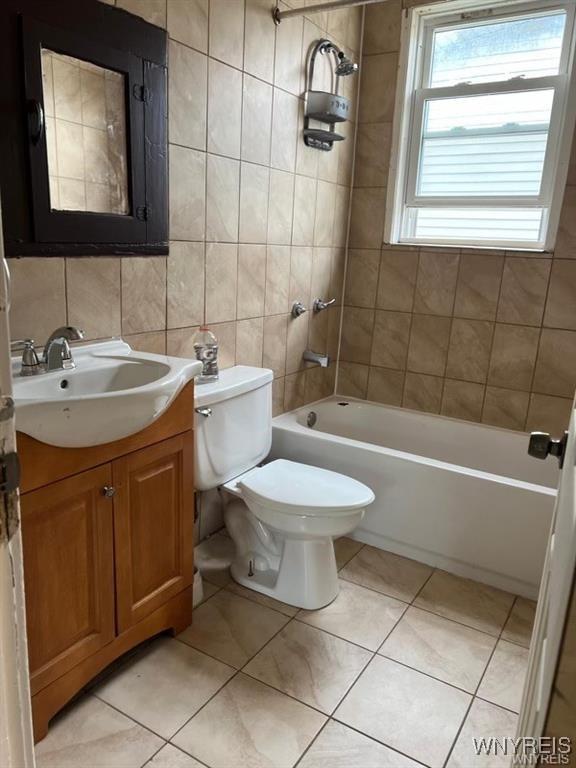 full bathroom with vanity, tile patterned flooring, tiled shower / bath combo, toilet, and tile walls