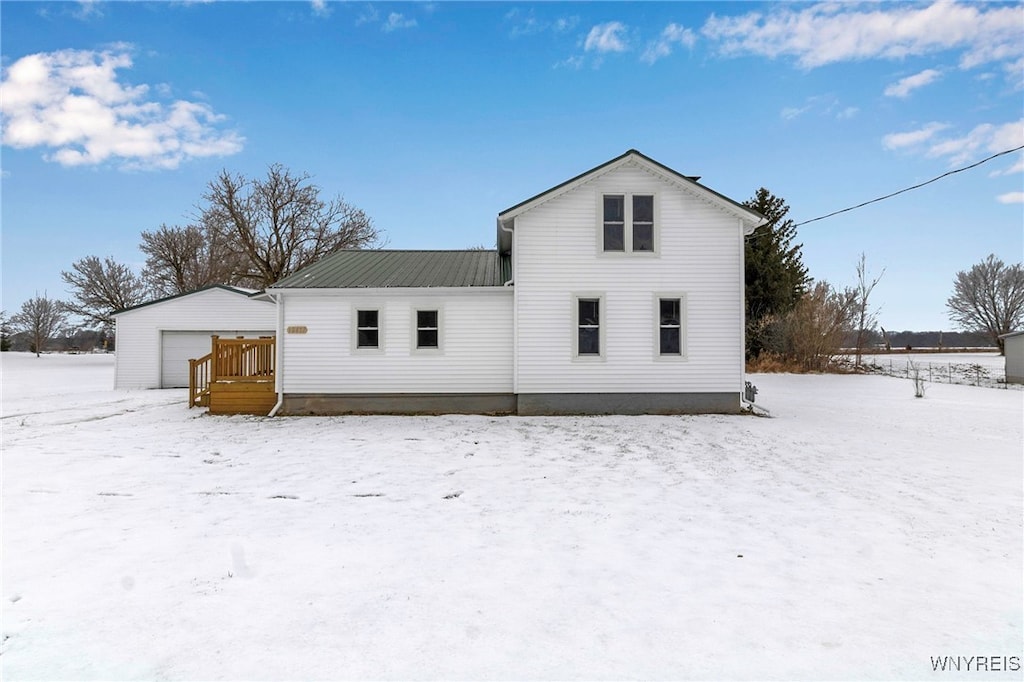 snow covered rear of property featuring a garage and an outdoor structure