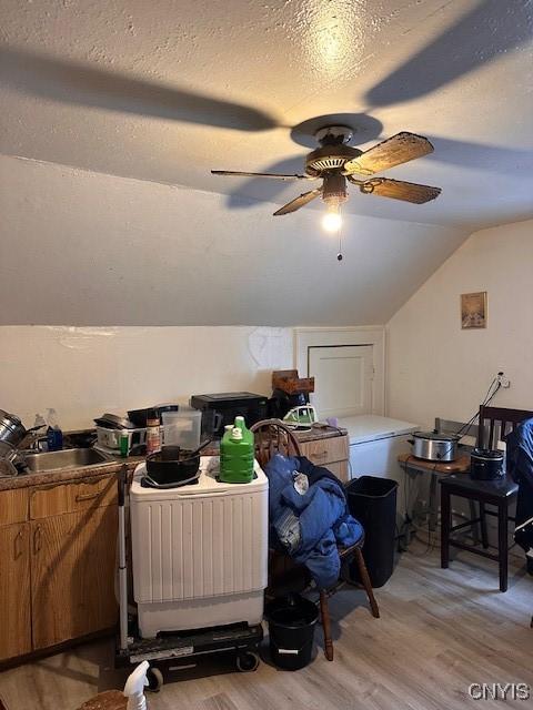 bonus room with a ceiling fan, light wood-style flooring, vaulted ceiling, a textured ceiling, and a sink