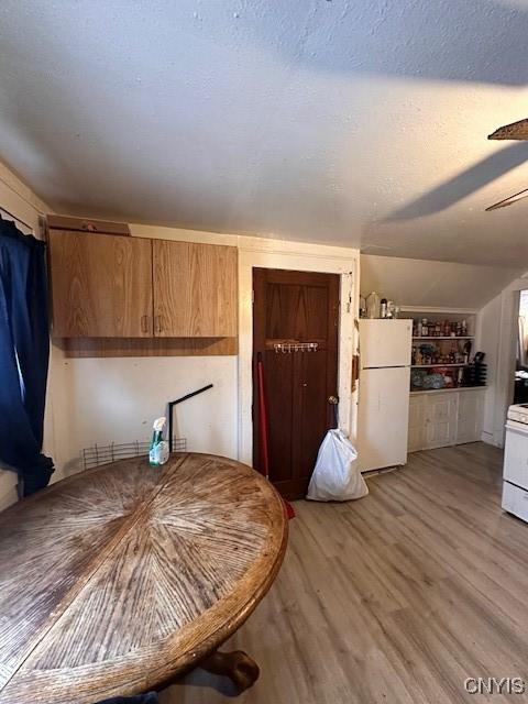 unfurnished dining area featuring light wood-style floors, vaulted ceiling, a textured ceiling, and a ceiling fan