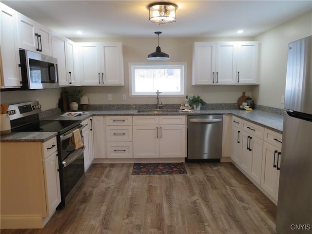 kitchen with white cabinetry, sink, hardwood / wood-style floors, decorative light fixtures, and appliances with stainless steel finishes