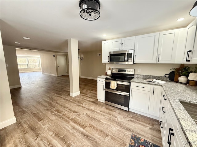 kitchen with white cabinets, appliances with stainless steel finishes, light hardwood / wood-style flooring, and light stone countertops