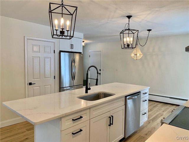 kitchen with sink, an island with sink, pendant lighting, stainless steel appliances, and white cabinets