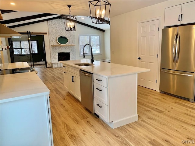 kitchen featuring sink, appliances with stainless steel finishes, hanging light fixtures, white cabinets, and a center island with sink