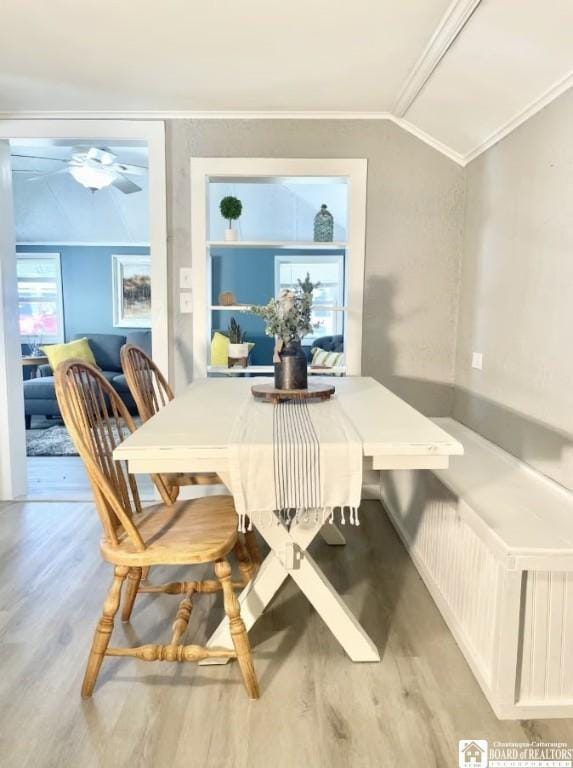 dining room featuring built in shelves, crown molding, vaulted ceiling, and light wood-type flooring