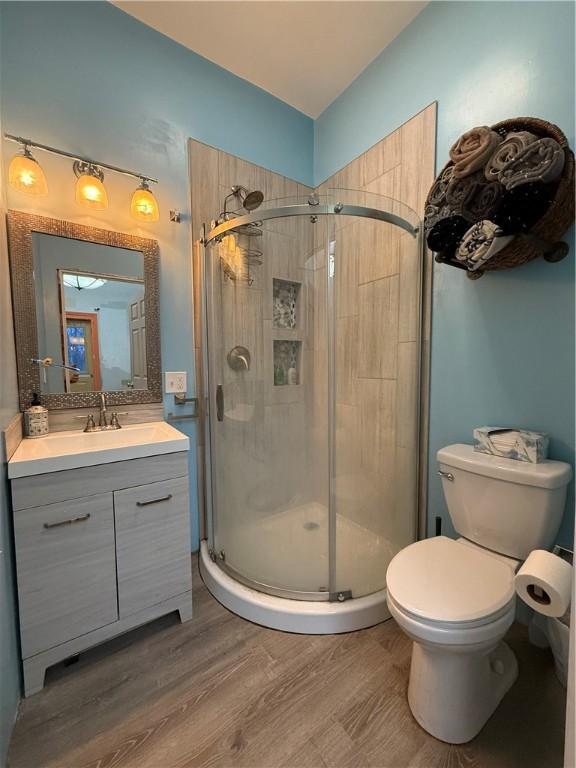 bathroom featuring hardwood / wood-style floors, vanity, toilet, and a shower with shower door