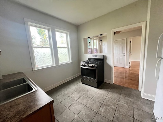 kitchen with light tile patterned floors, white refrigerator, stainless steel gas range oven, and sink