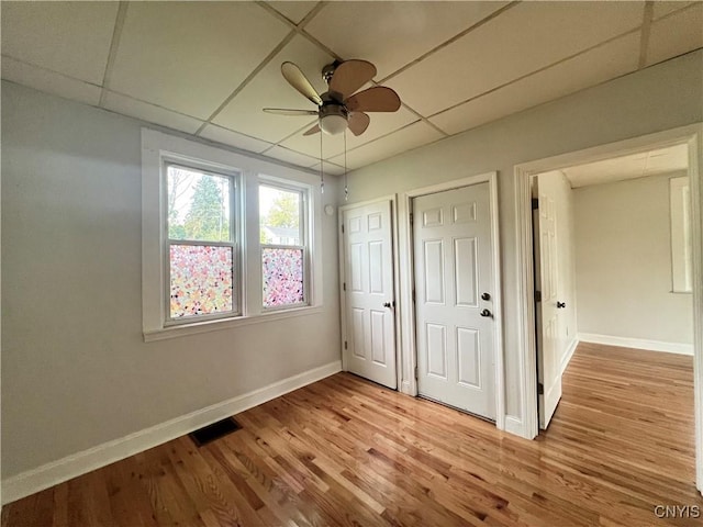 unfurnished bedroom with ceiling fan, a drop ceiling, and light hardwood / wood-style floors