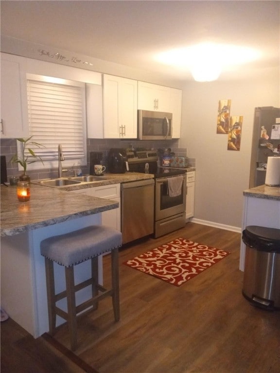 kitchen with white cabinetry, sink, stainless steel appliances, dark hardwood / wood-style floors, and a breakfast bar area