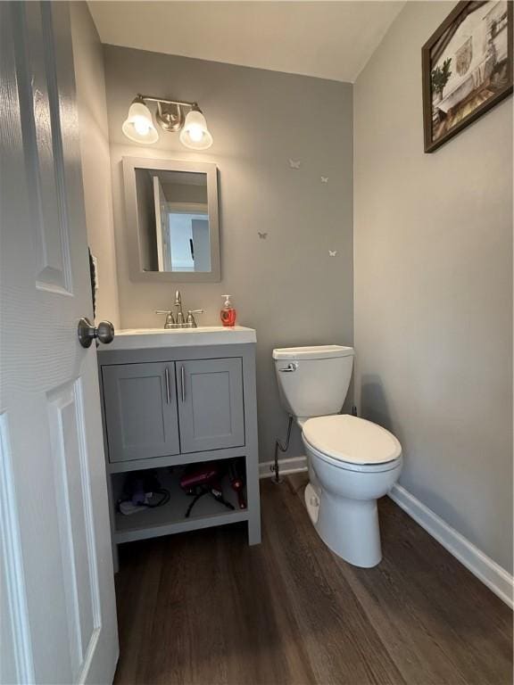 half bath featuring wood finished floors, baseboards, toilet, and vanity