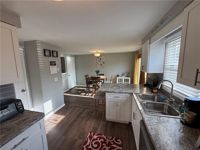 kitchen featuring a sink, dark wood-type flooring, a peninsula, white cabinetry, and baseboards