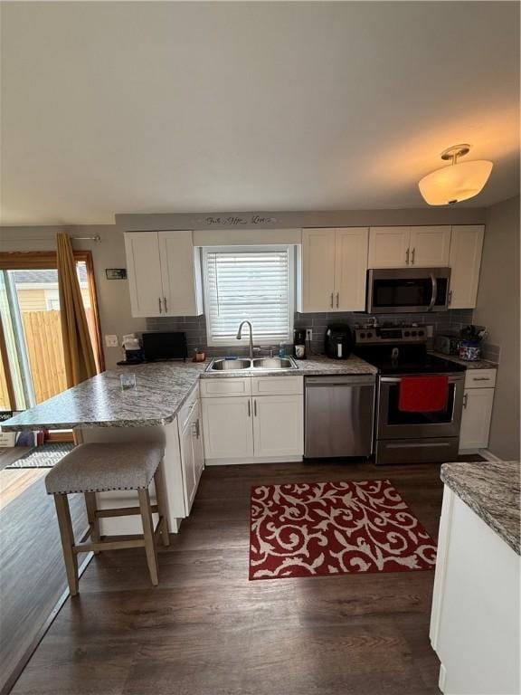 kitchen featuring stainless steel appliances, a sink, white cabinetry, and a peninsula