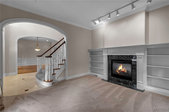 unfurnished living room with built in shelves, crown molding, a premium fireplace, and carpet floors